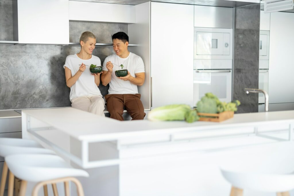 Laughing couple eating salad on kitchen at home